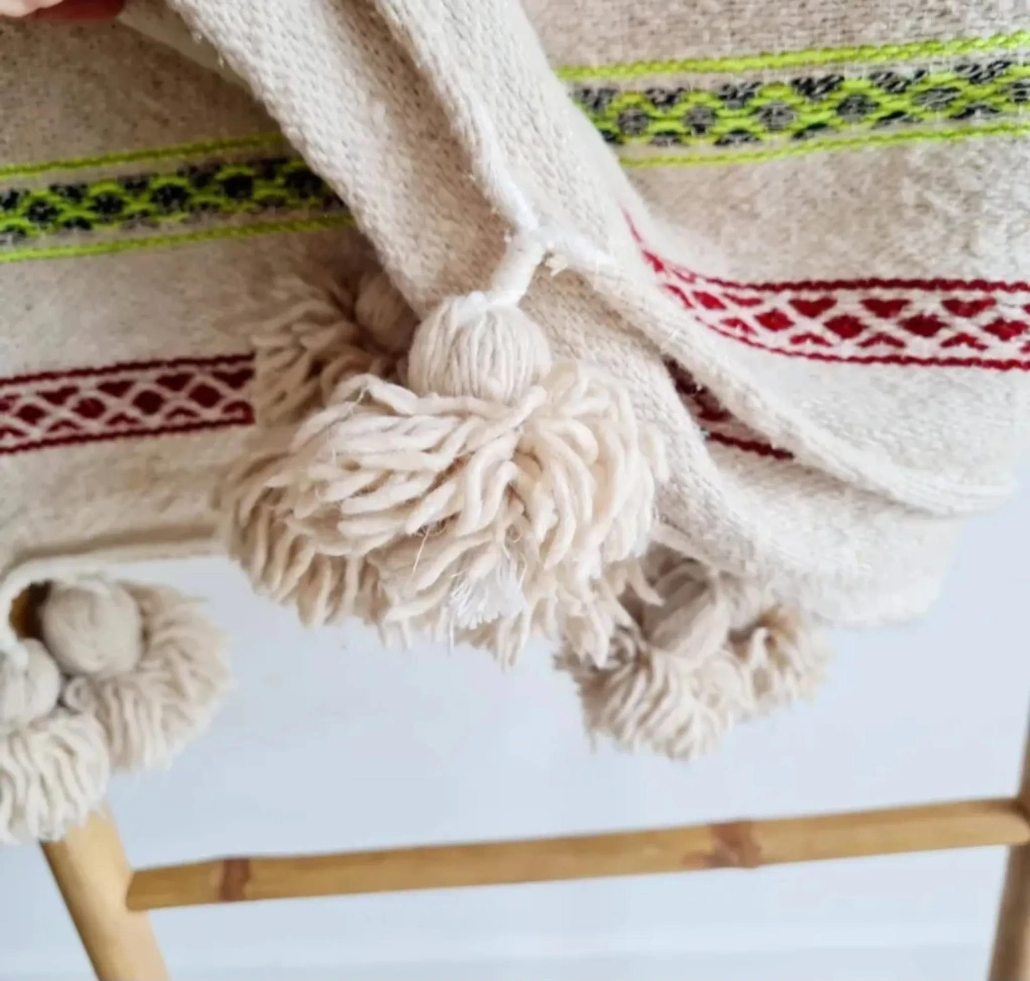 Moroccan plaid made of handwoven wool, decorated with stripes and pom-poms.