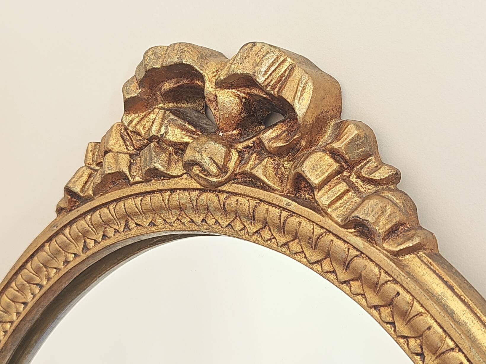 Vintage oval mirror with a carved wooden frame in gold, decorated with a bow.
