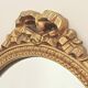 Vintage oval mirror with a carved wooden frame in gold, decorated with a bow.