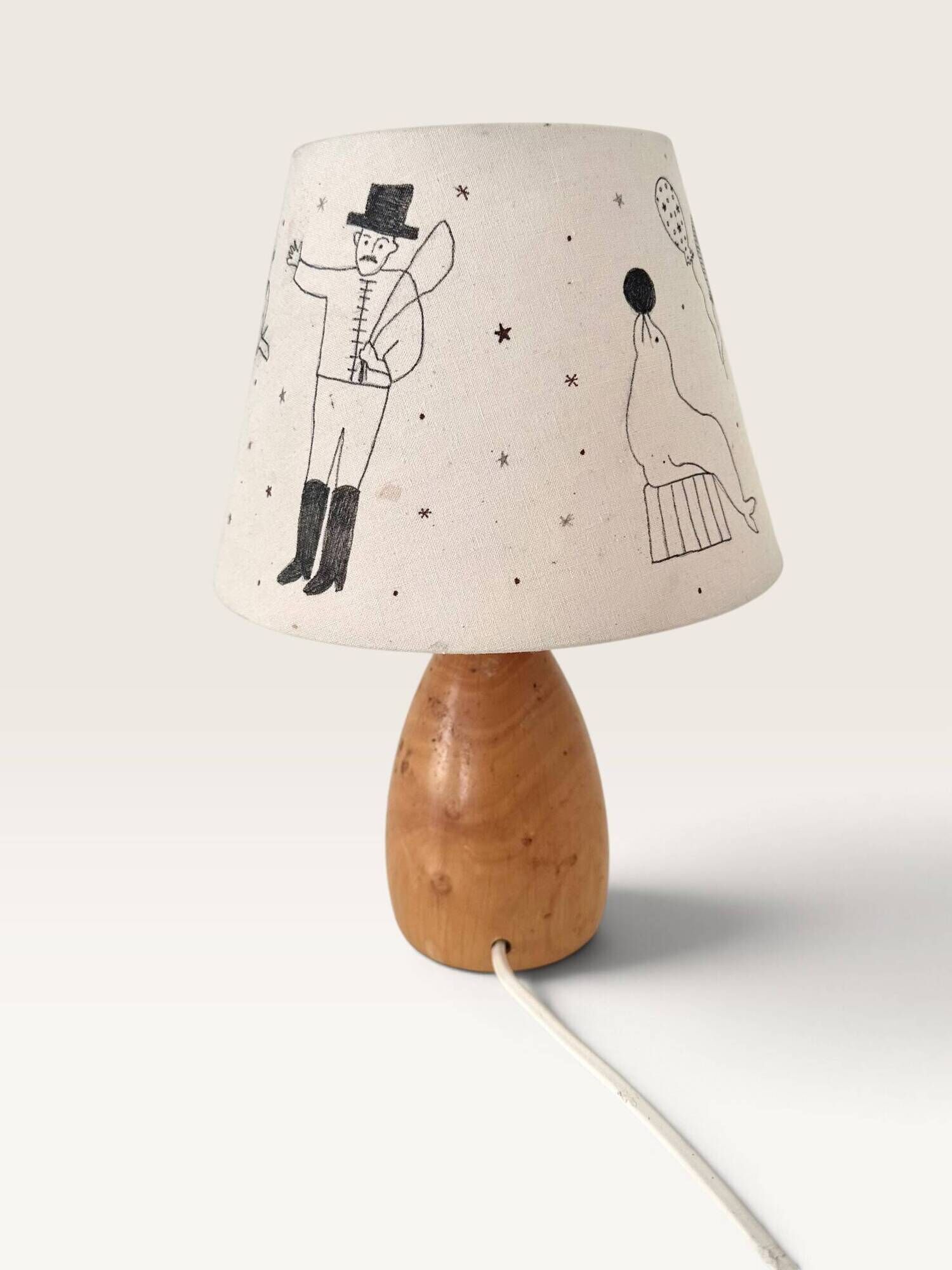 Wood-turned lamp with a hand-drawn lampshade, circus patterns.