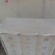 A beautifully crafted crossbow-shaped chest of drawers, finished in pearl grey with a whitewashed top.