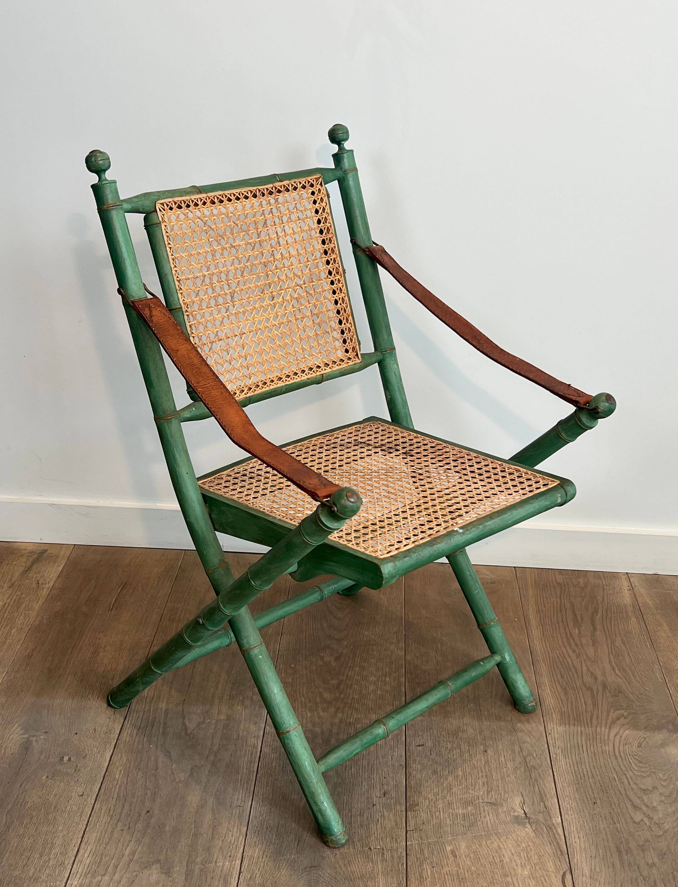 Paire de chaises safari pliantes façon faux-bambou patiné, dossiers et assises cannées et repose-bras en cuir
