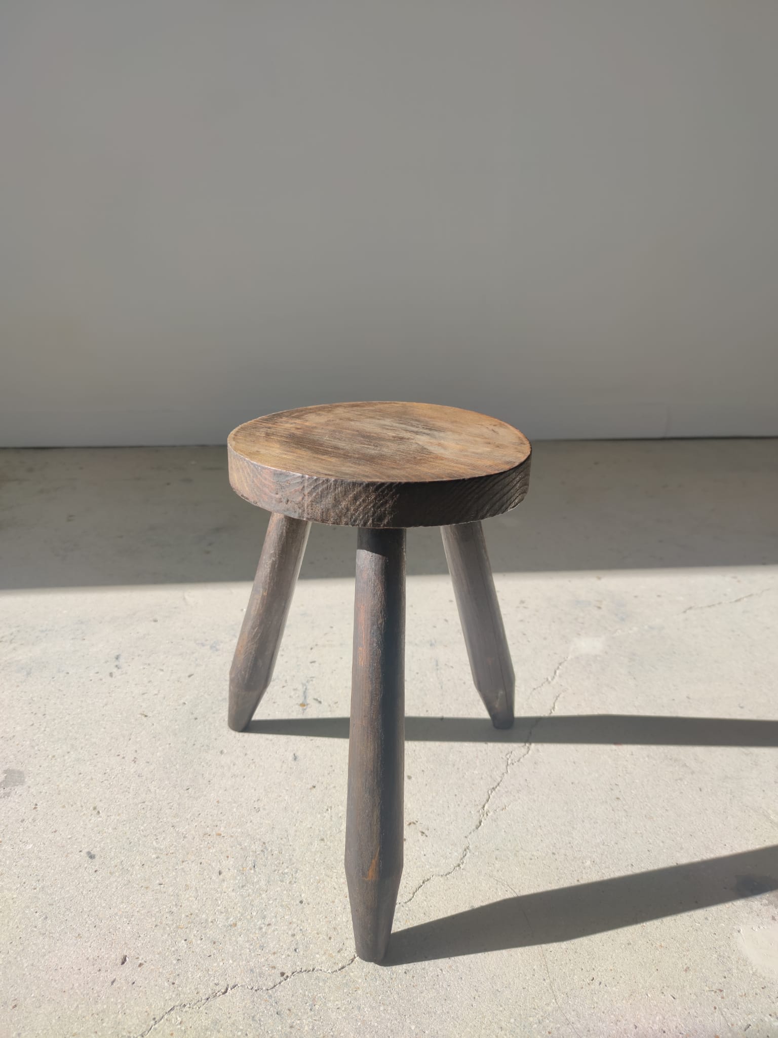 Small brutalistic tripod stool in dark wood tapered feet circular seat