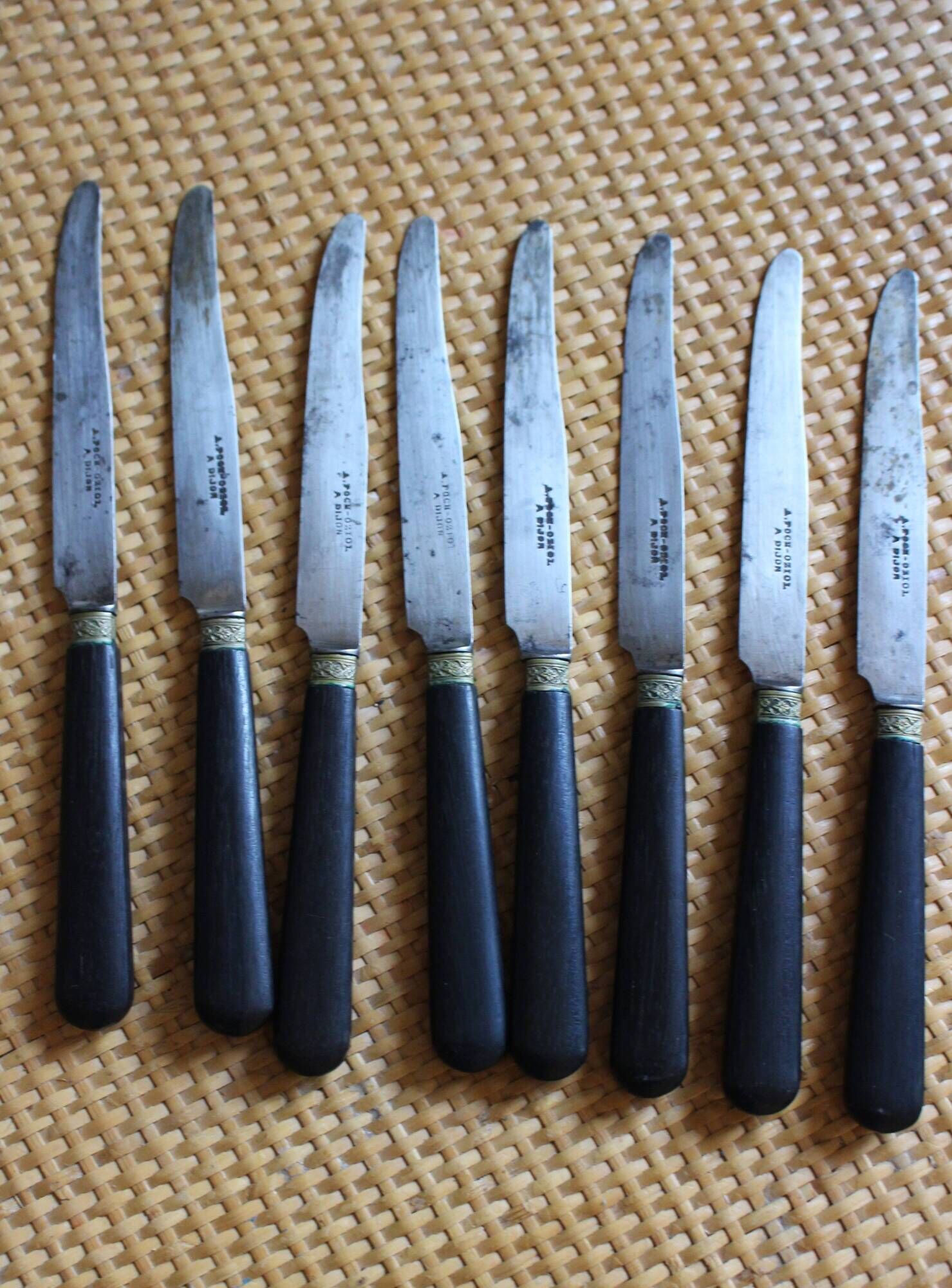 A set of 8 knives with black wooden handles and bolsters.