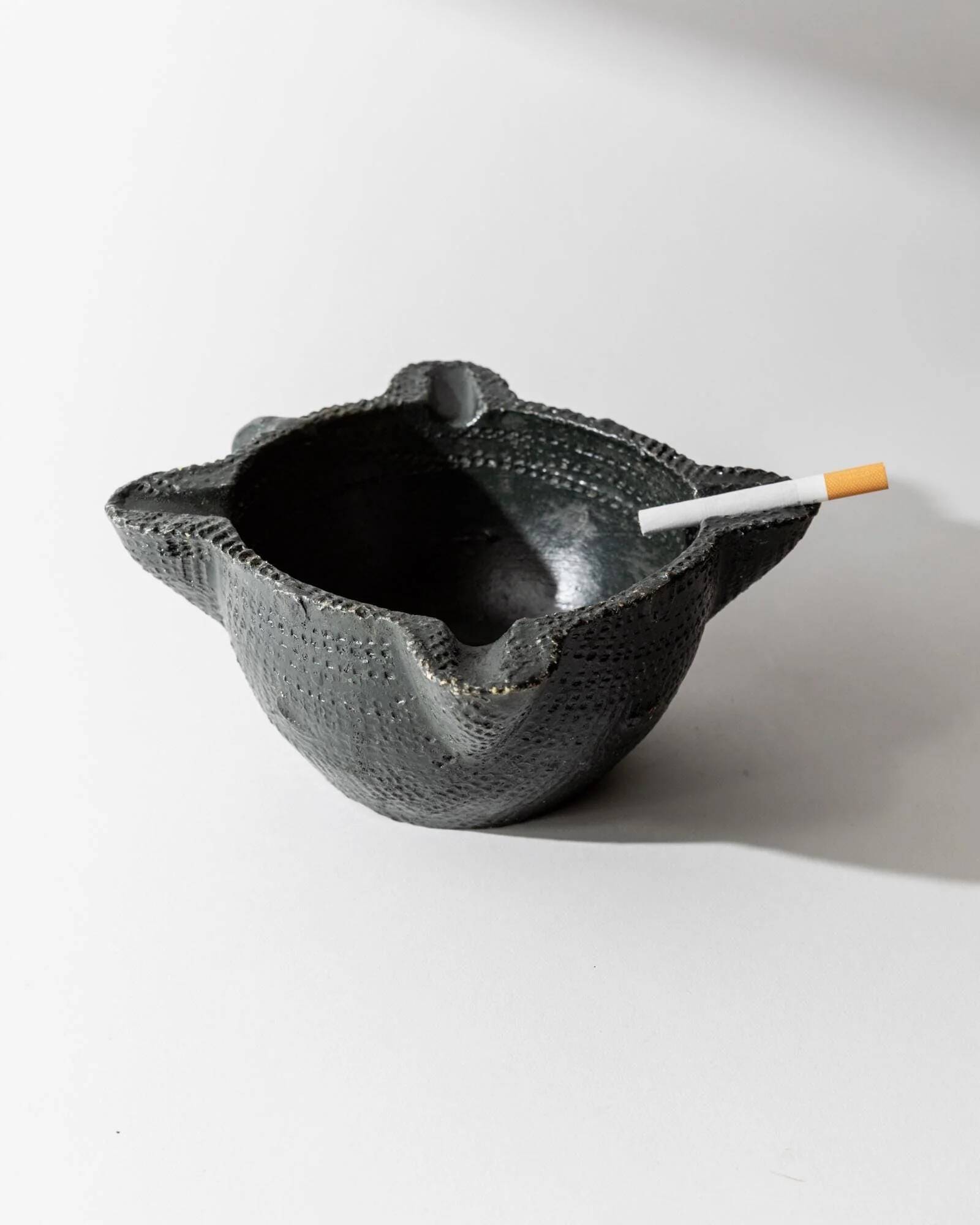 Vintage ceramic ashtray from the 1960s, black, hand-sculpted texture, organic shape.