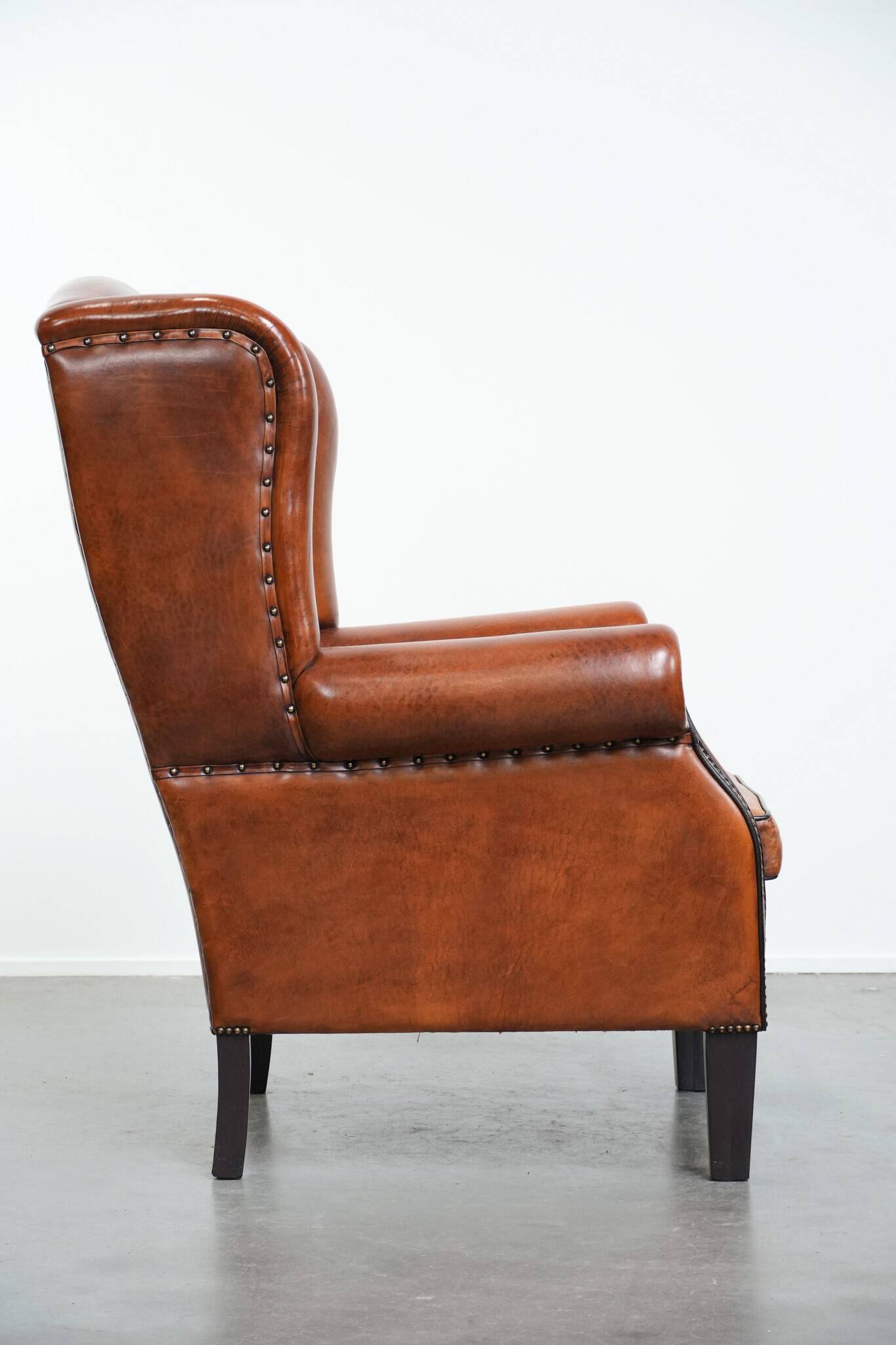 Large sheepskin wingback chair with black piping and decorative nails
