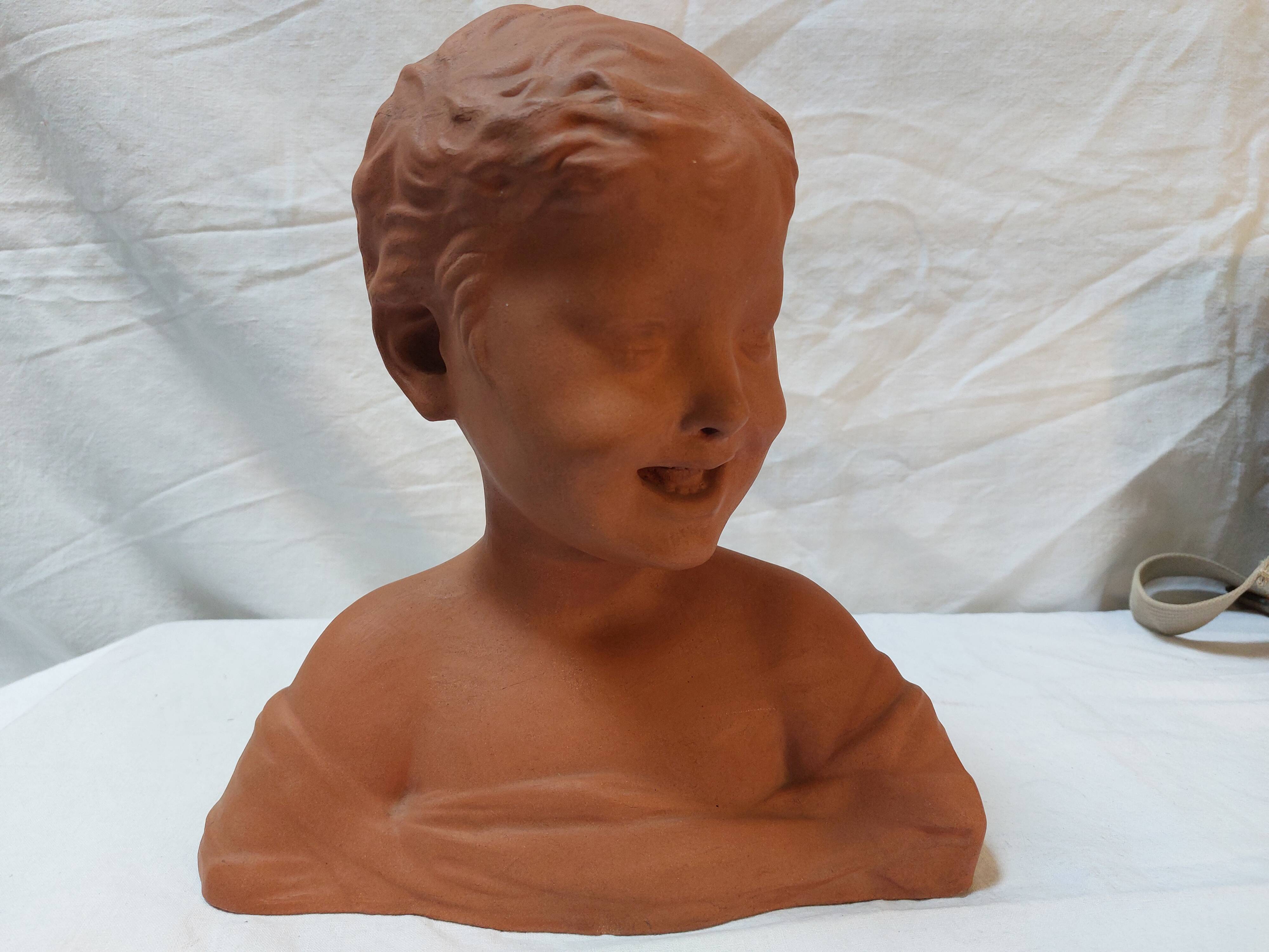 Terracotta bust of a smiling little boy.