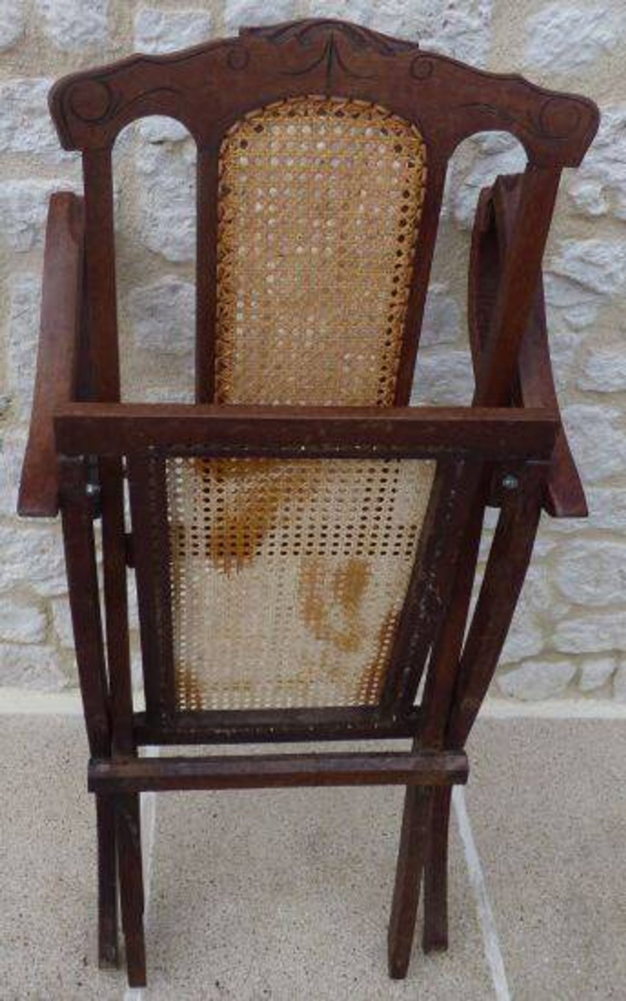Antique folding chair with caned seat and backrest made of wood.