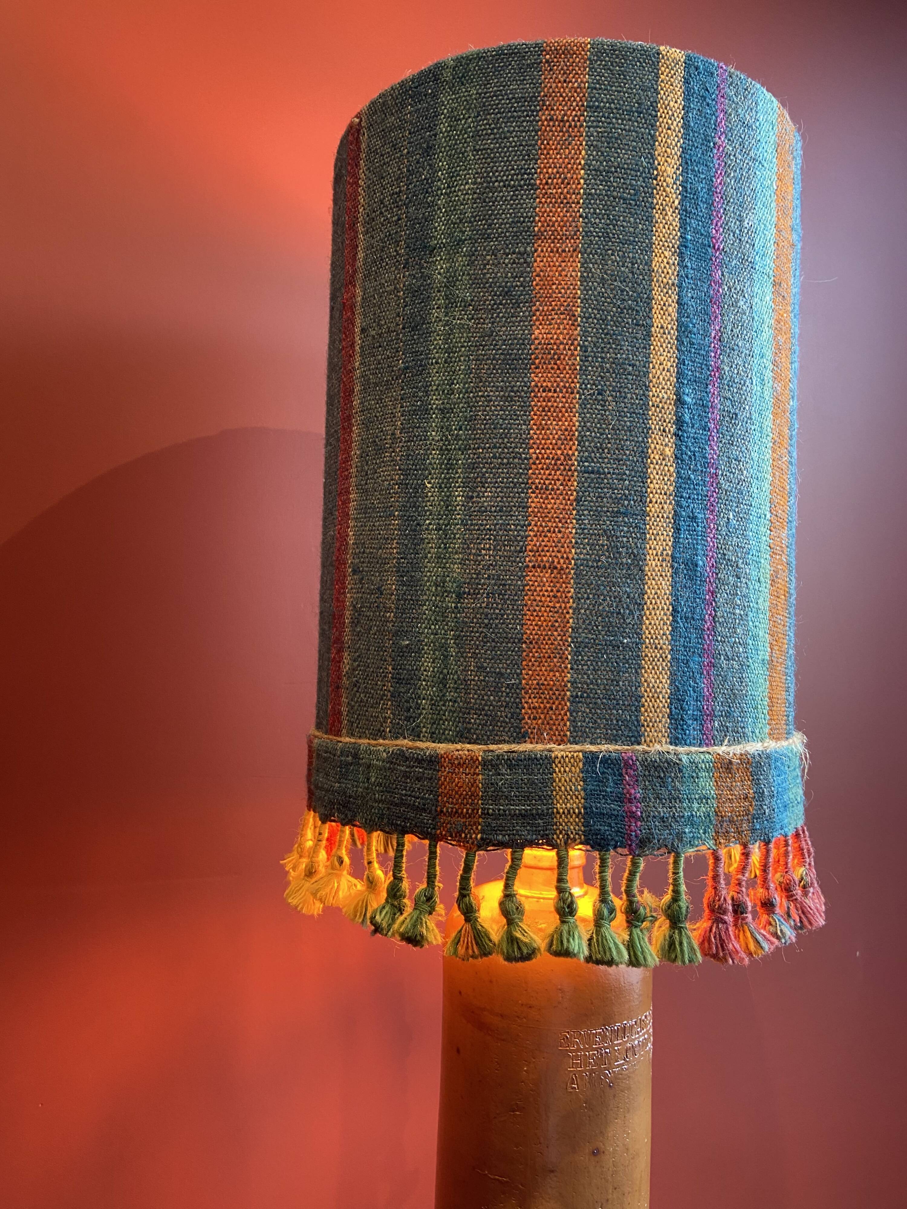 "Stoneware Bottle Lamp" with a multicoloured blue lampshade handwoven in India.