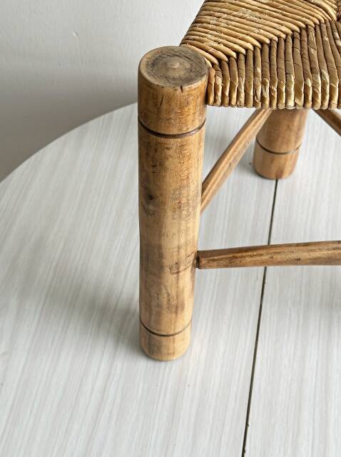 Antique tripod stool in light wood with a woven straw seat.