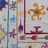 White suzani kilim rug with multi-colored embroidered patterns