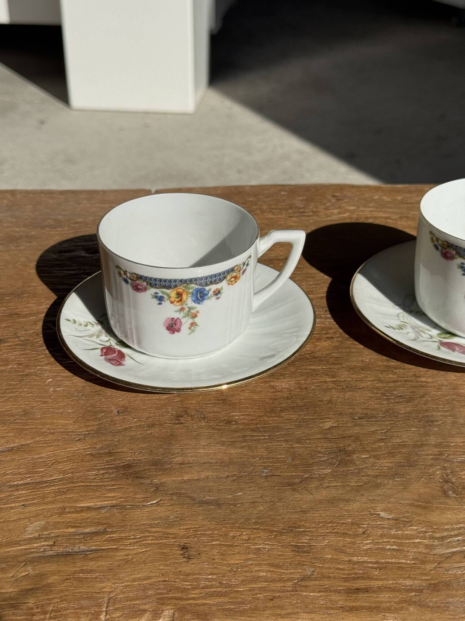 Pair of white porcelain cups from ADP France with a floral pattern and their s