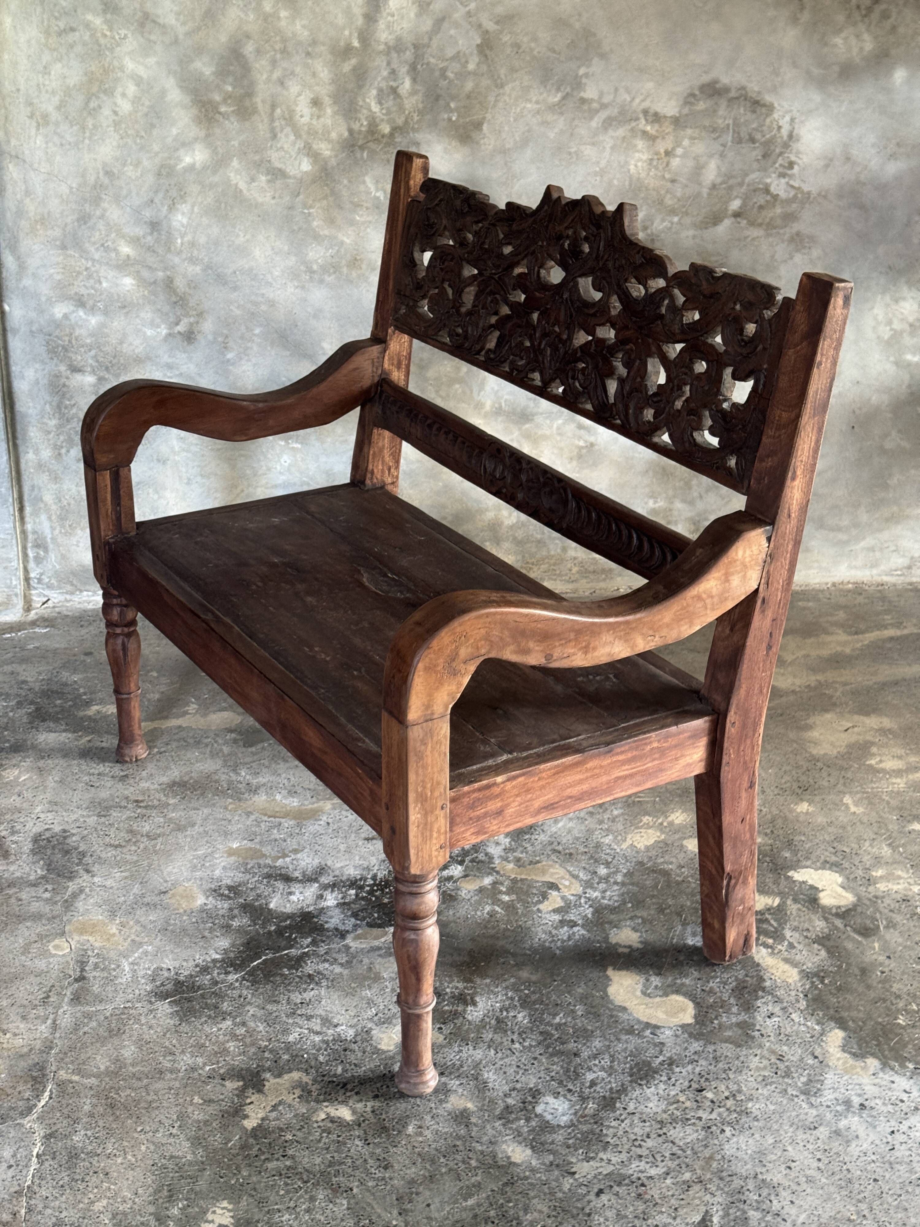Small antique Indonesian bench in carved teak with plant and floral motifs.