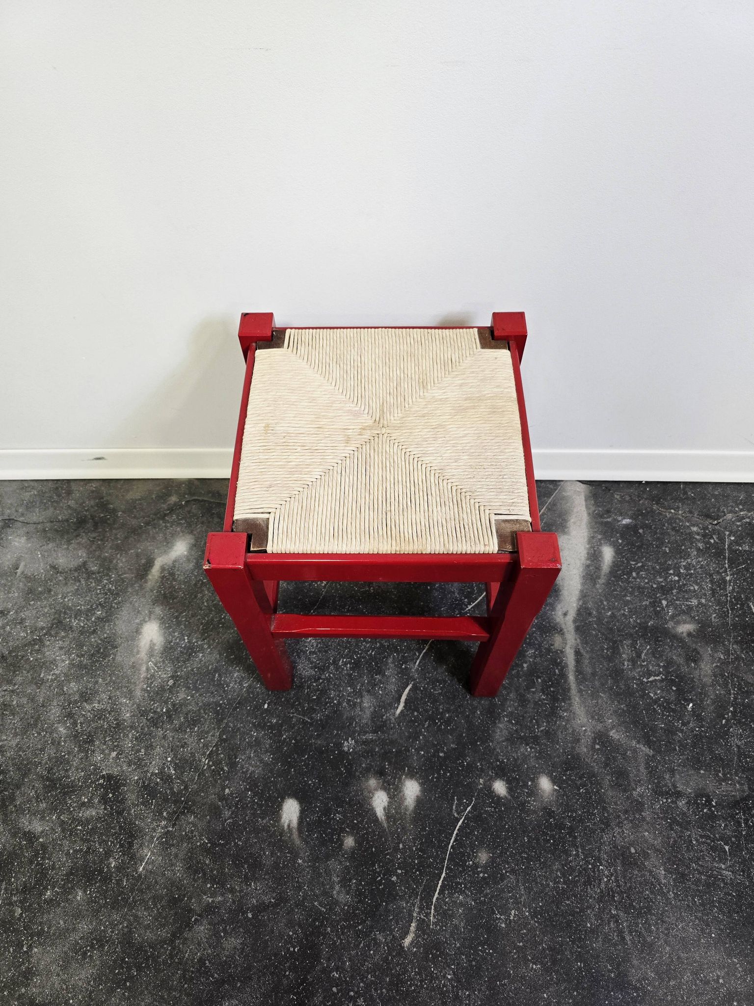 Red wooden stool with a woven straw seat.