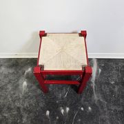 Red wooden stool with a woven straw seat.