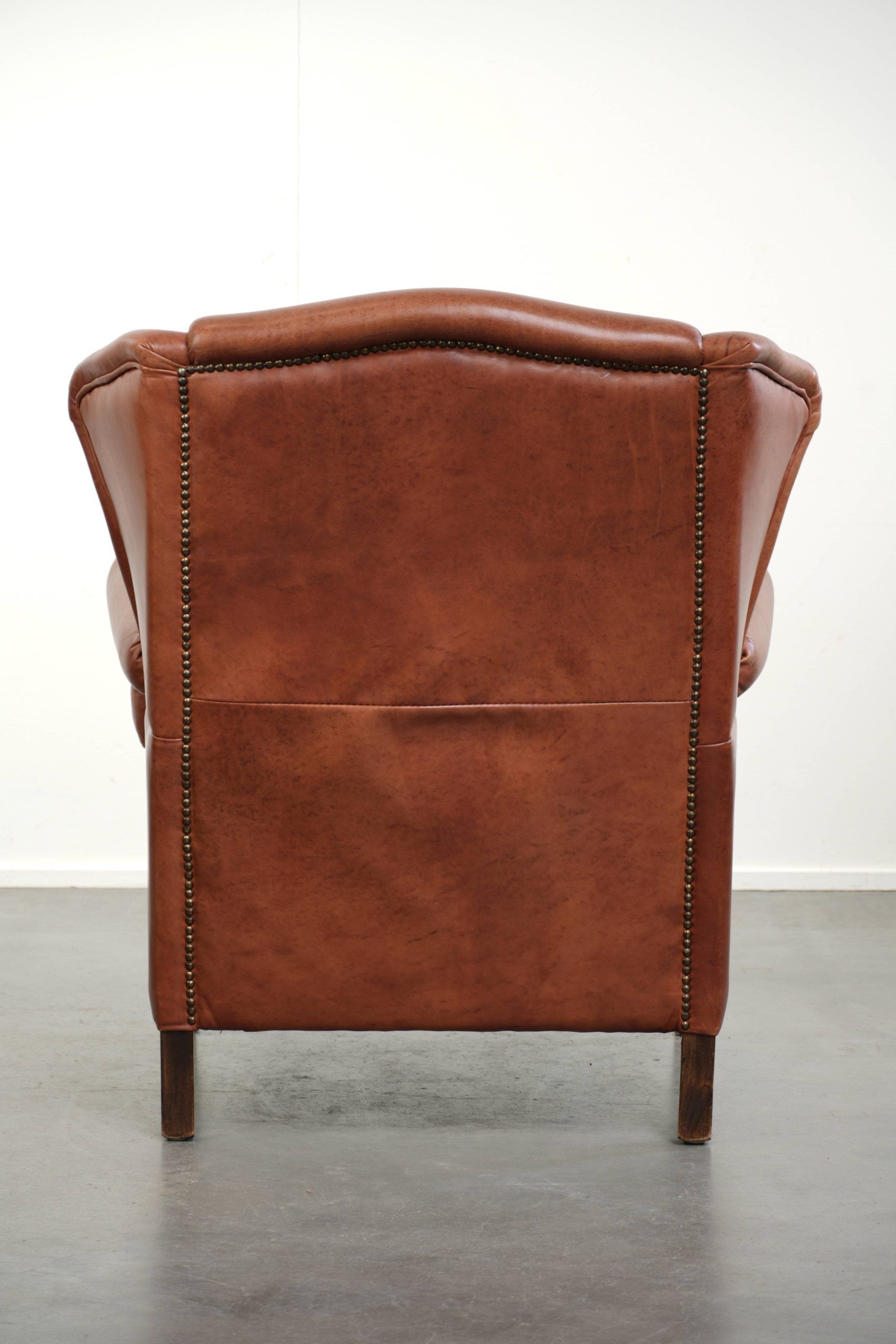 Light cognac-coloured cow leather wingback armchair with matching piping