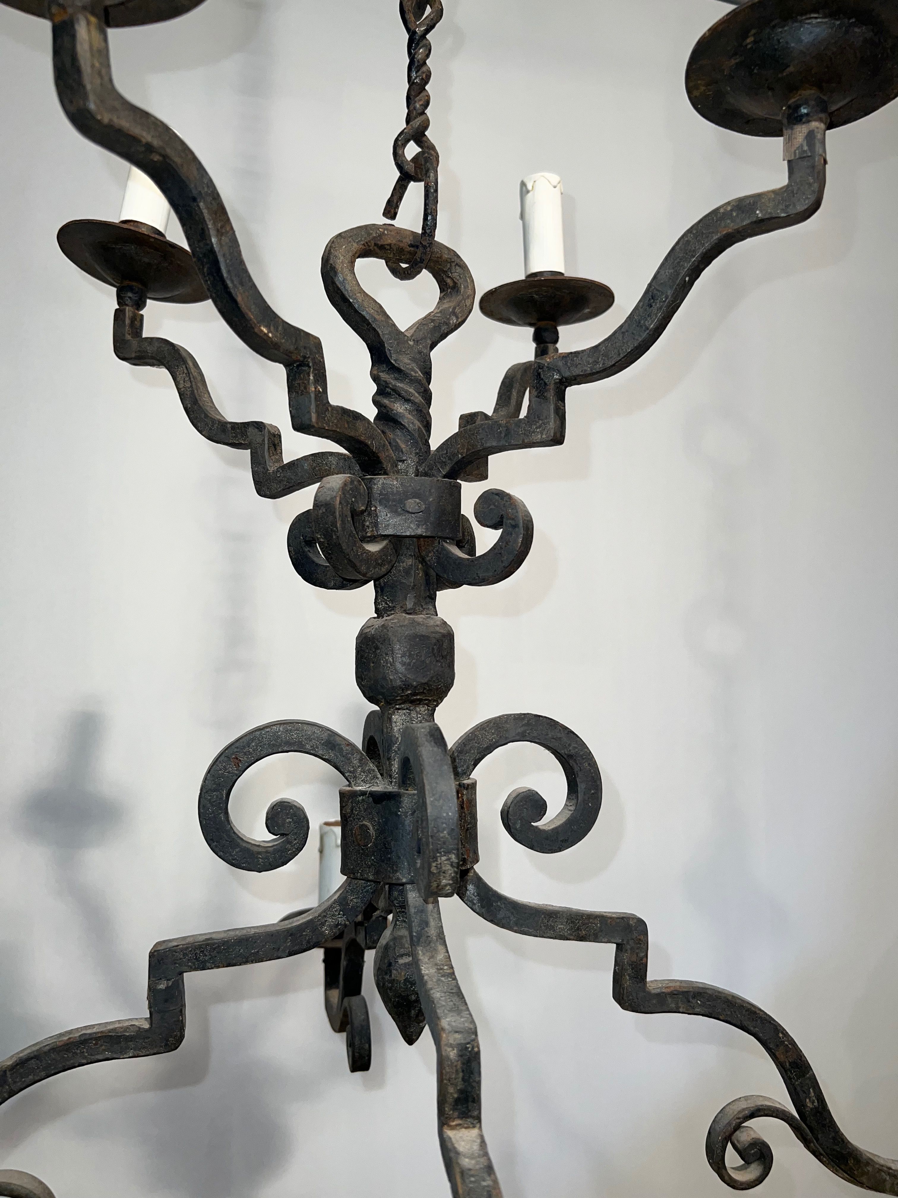 Two-tiered wrought iron chandelier with eight light arms in Gothic style.