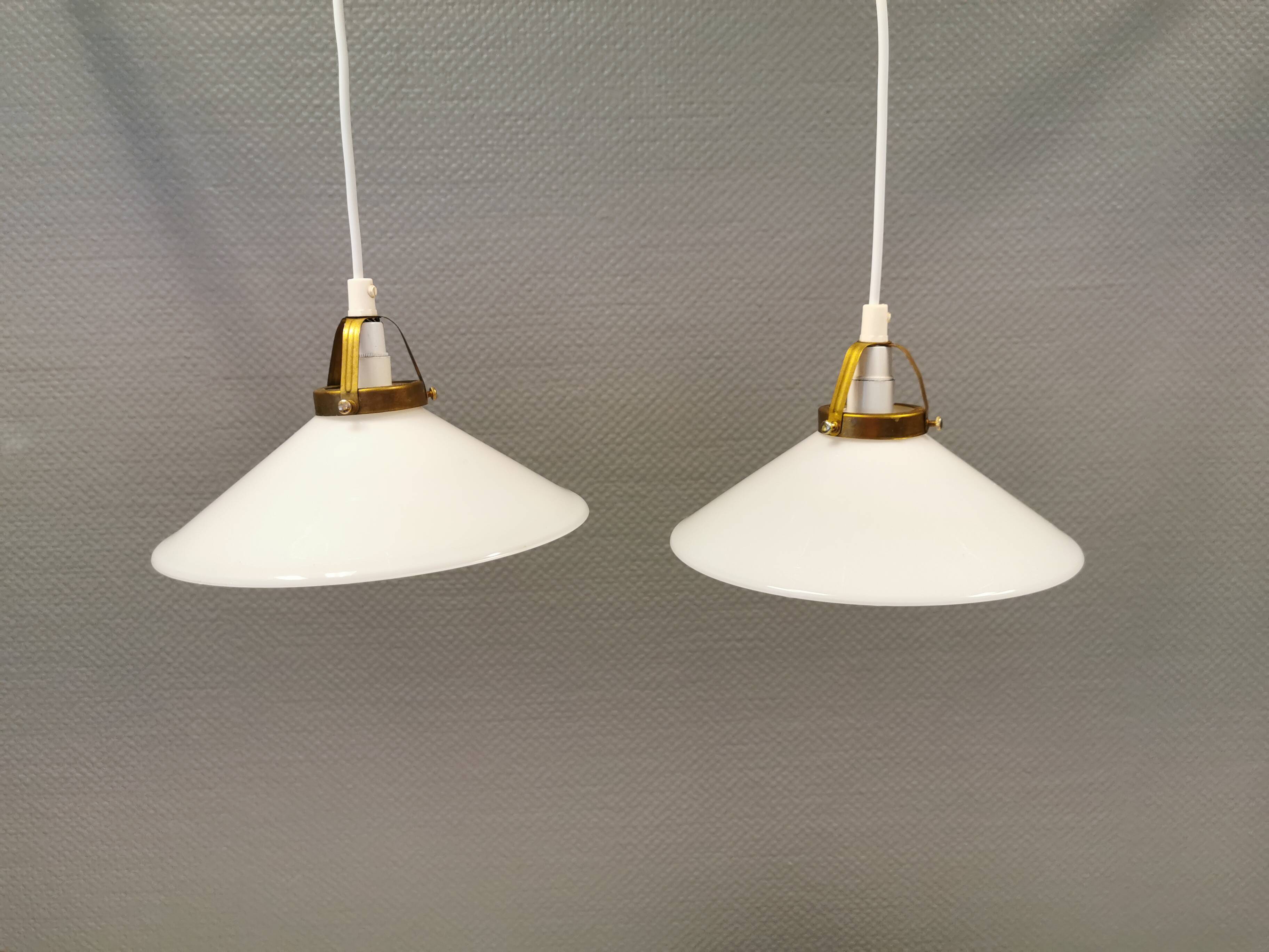 A set of hanging lamps in milky white opal glass with brass top.