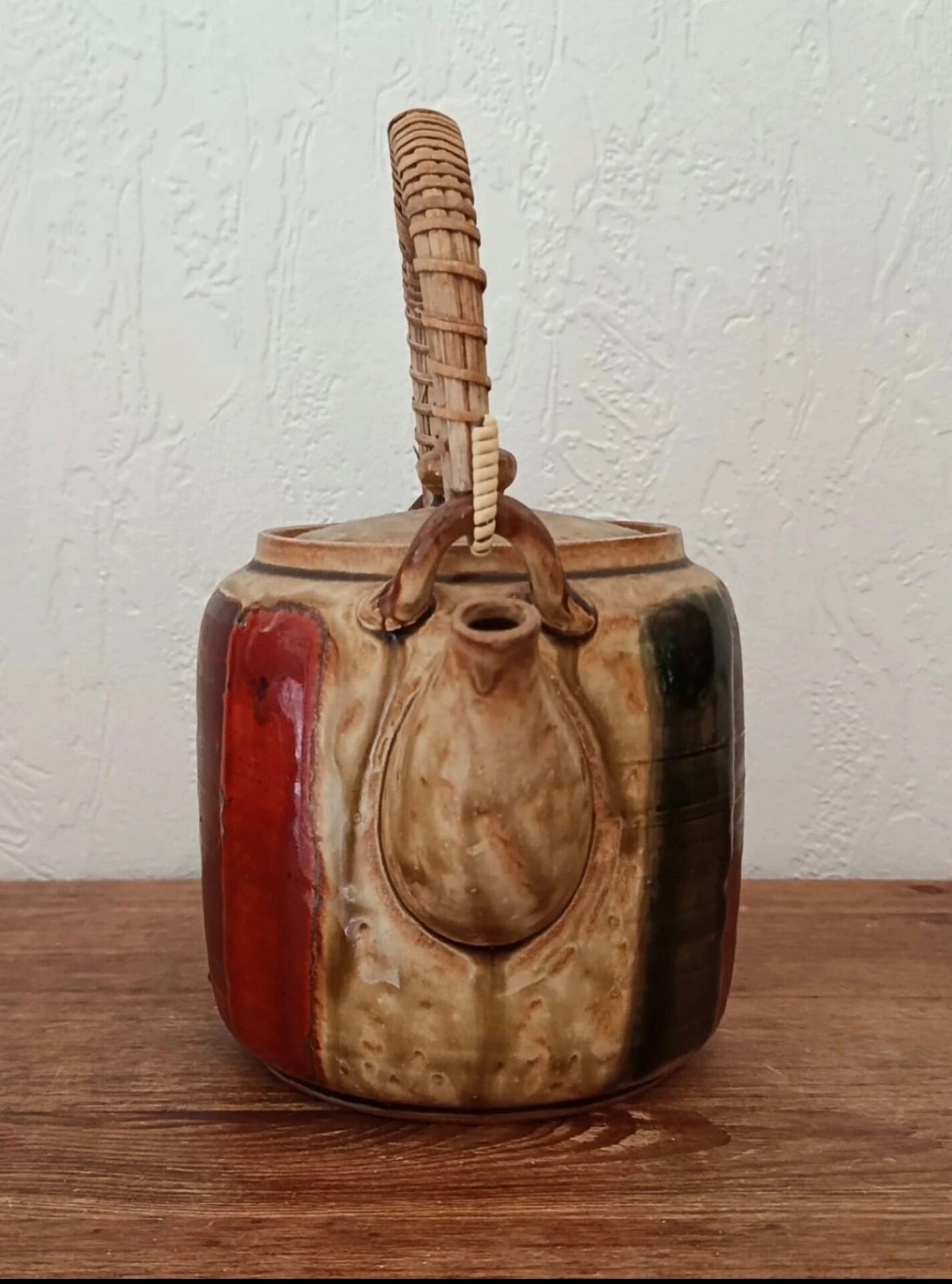 Vintage ceramic teapot with an enamel finish, rattan handle, warm tones.