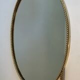 Oval brass mirror surrounded by a cord and adorned