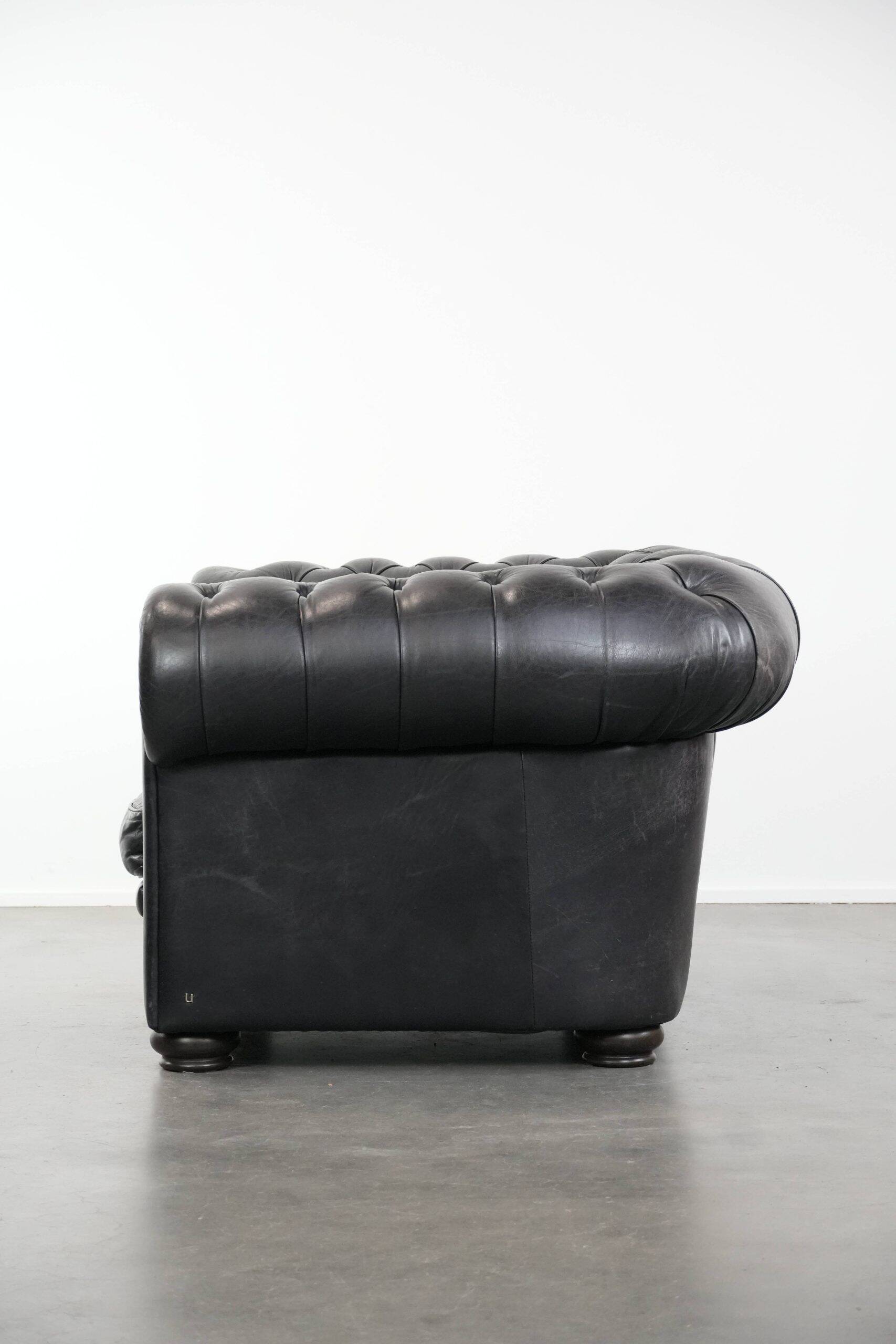 Ensemble composé d'un canapé chesterfield noir, d'un fauteuil et d'un pouf.