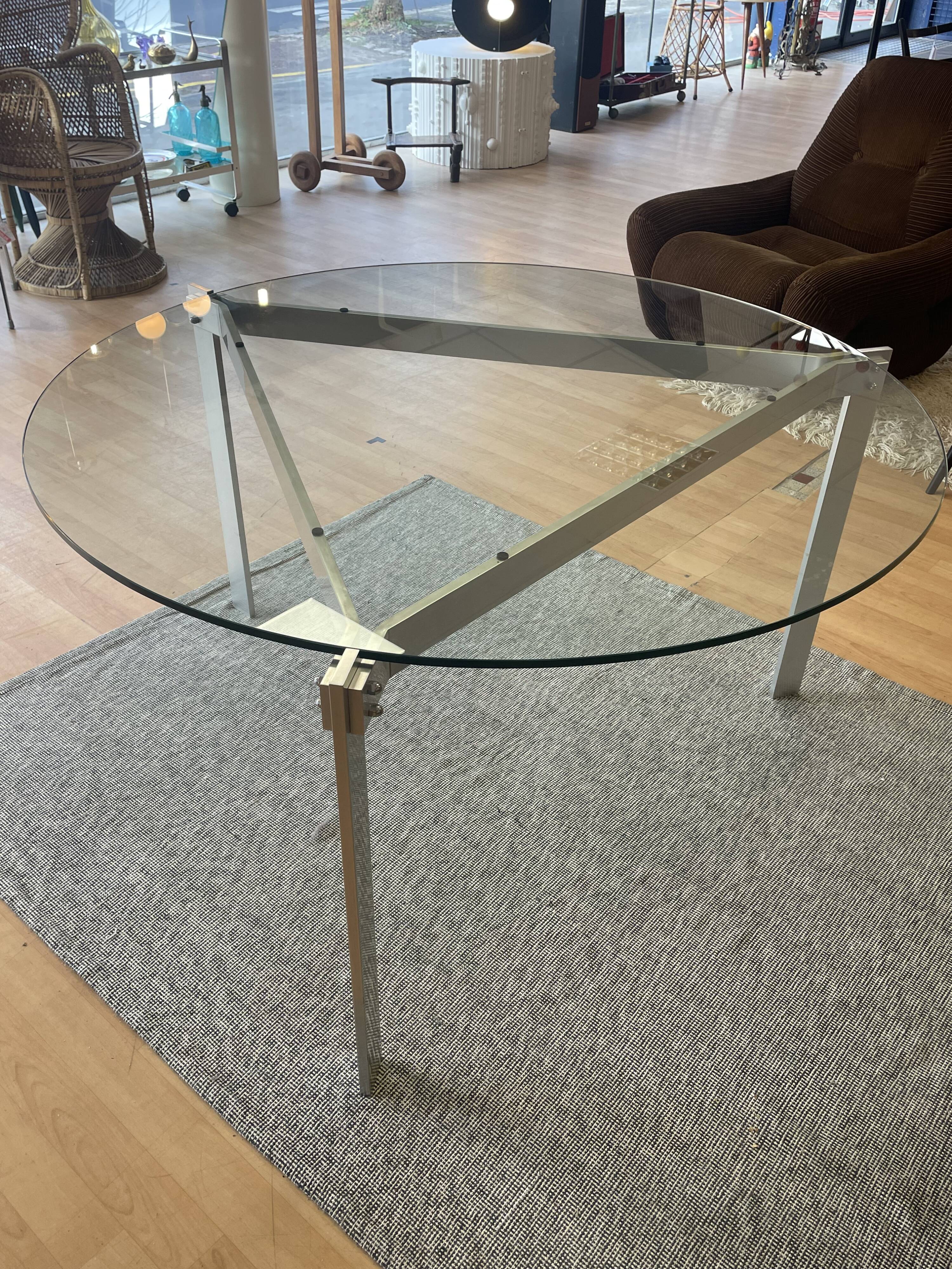 Round dining table with a glass top and brushed metal triangular frame.