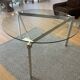 Round dining table with a glass top and brushed metal triangular frame.