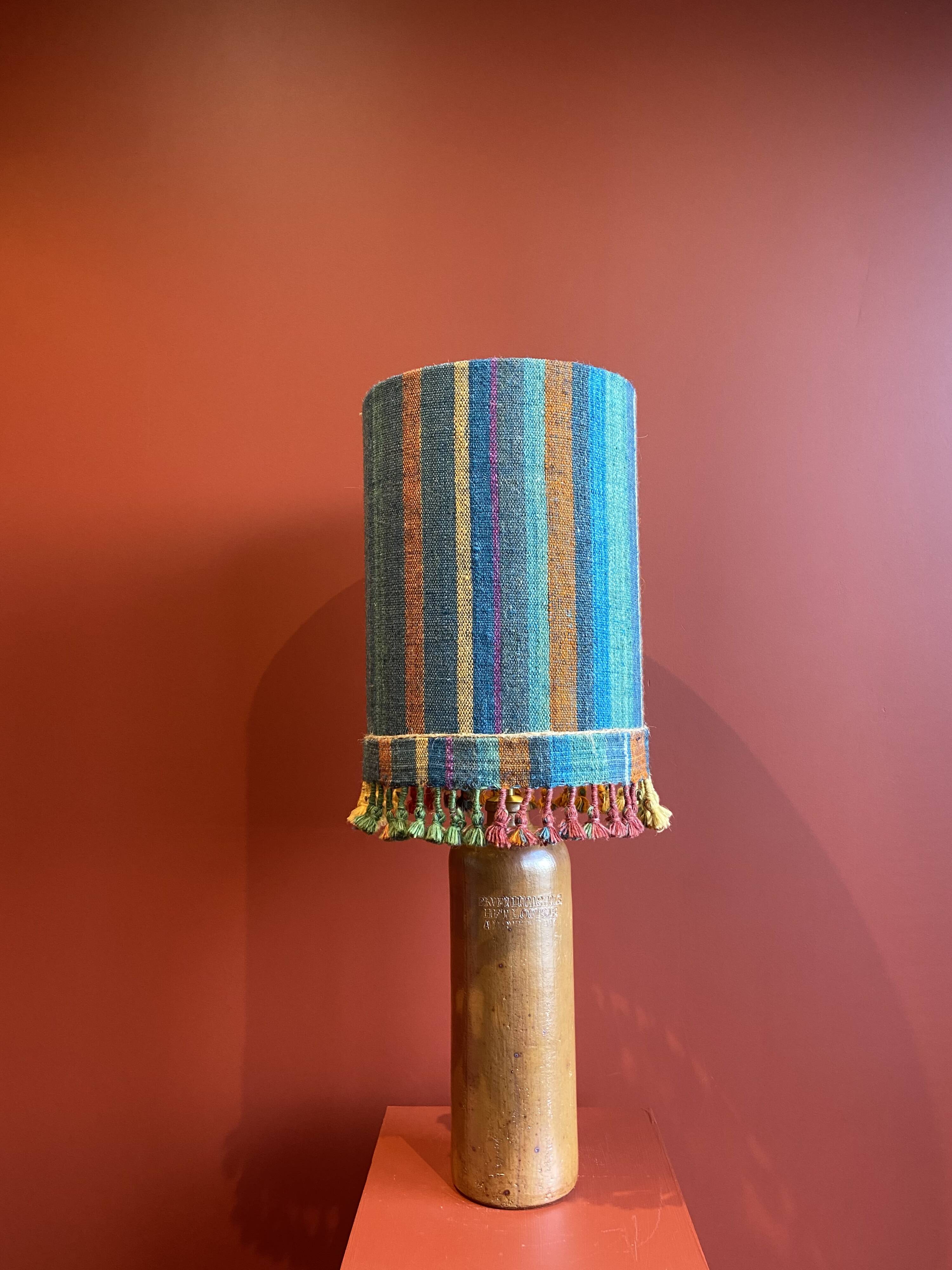 "Stoneware Bottle Lamp" with a multicoloured blue lampshade handwoven in India.