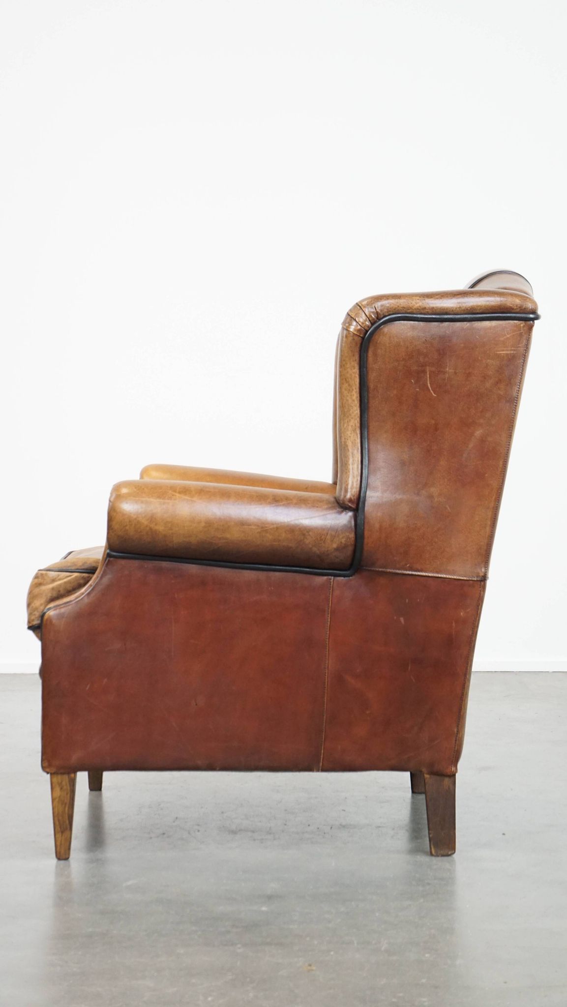Cognac-colored sheep leather wingback chair finished with black piping