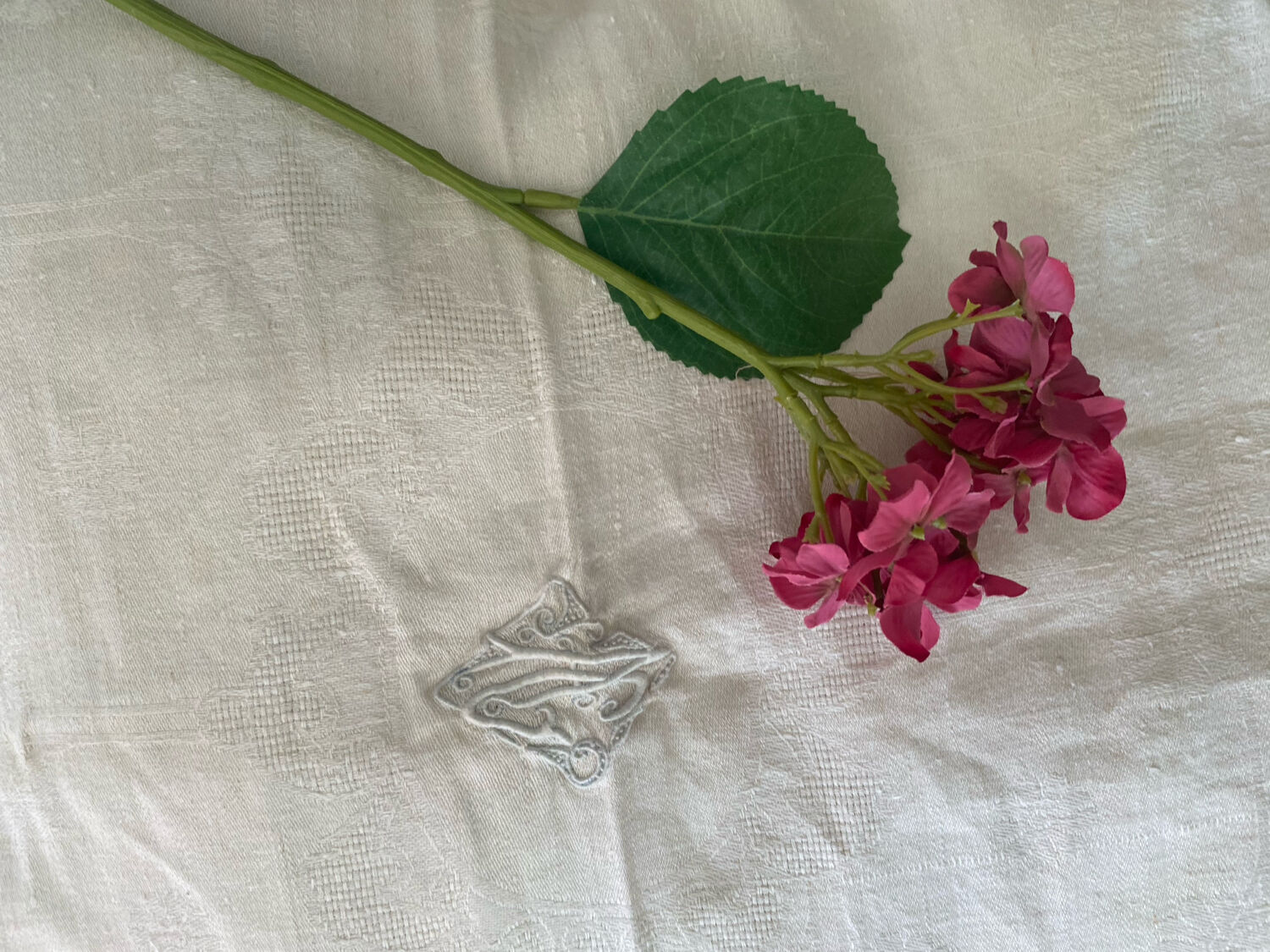 Damask tablecloth with a floral pattern and a central embroidered monogram.