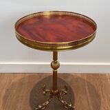 A round, neoclassical-style brass side table with a base decorated with dolphins and a red celluloid top encircled by an openwork gallery, attributed to the House of Jansen.