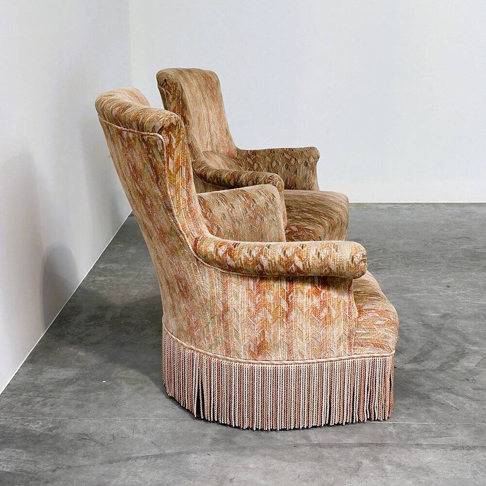Pair of sculptural Hollywood Regency lounge chairs with original fringed upholstery