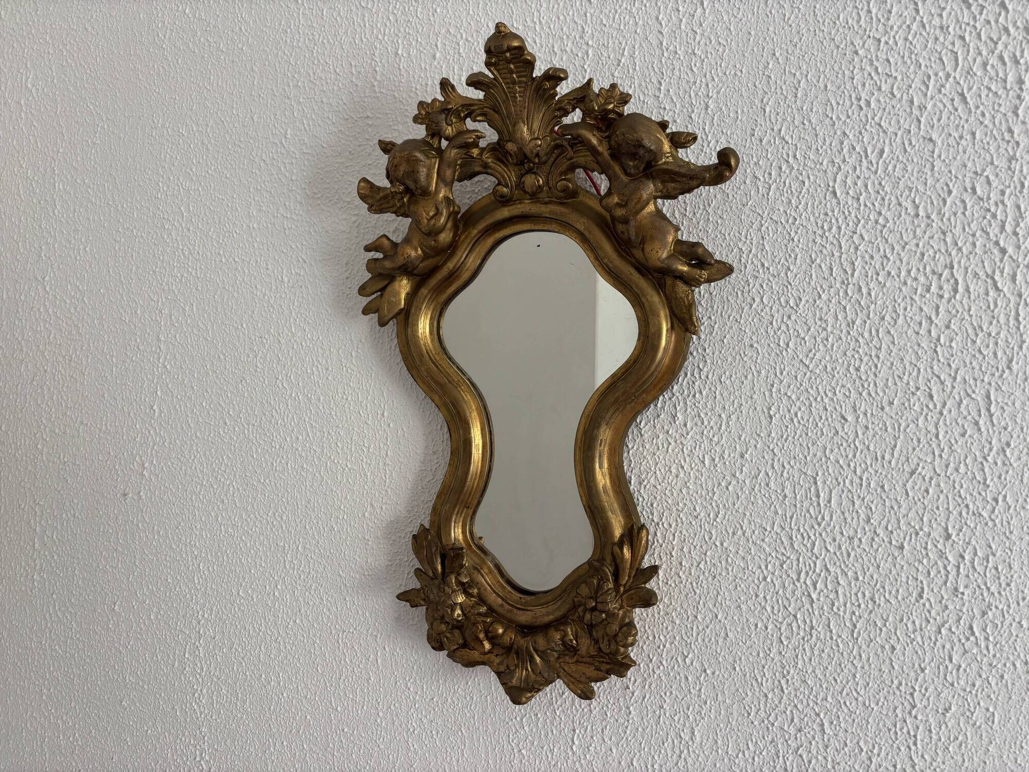 Antique rococo mirror with putti, gilded carved wood and stucco frame, 19th century.