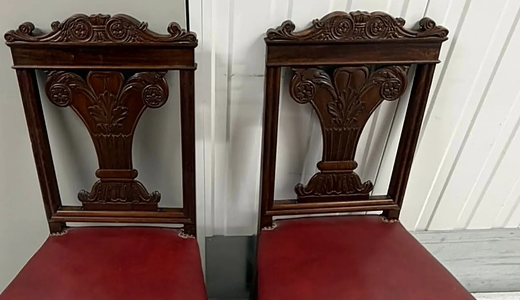 Pair of carved mahogany chairs with red faux leather seats.