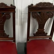 Pair of carved mahogany chairs with red faux leather seats.