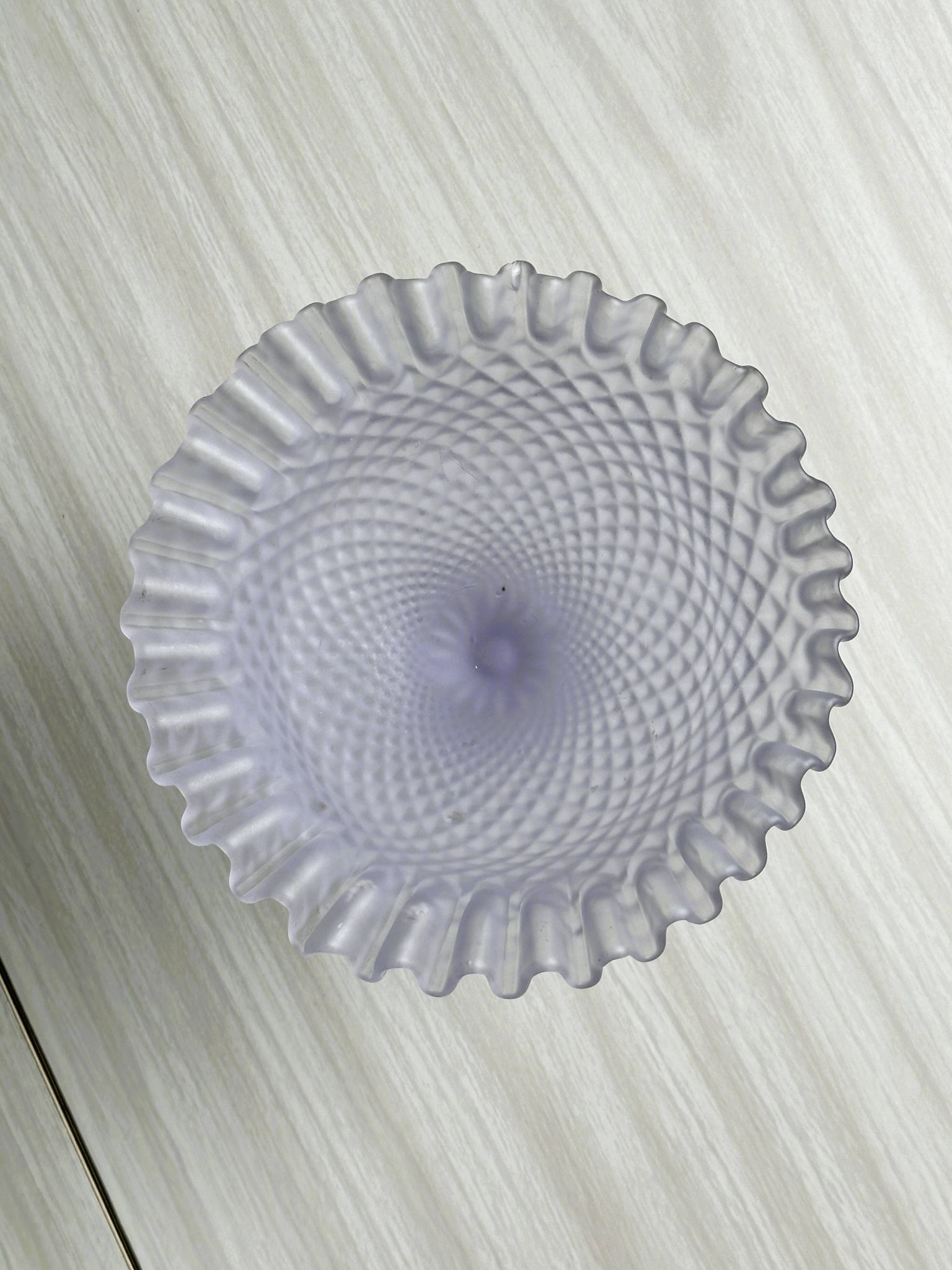 Purple glass pedestal bowl with wavy border and relief pattern.