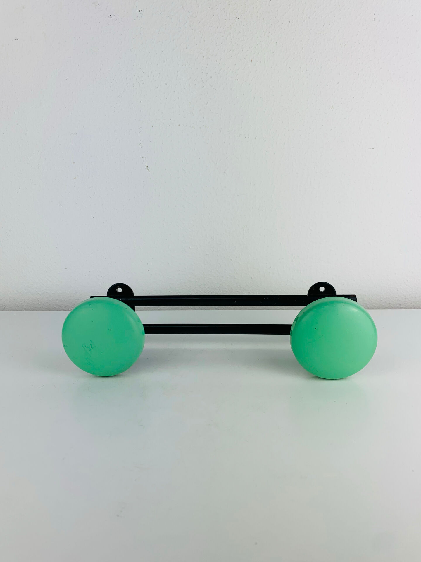 Wall-mounted coat rack with 2 green hooks from the 1950s.