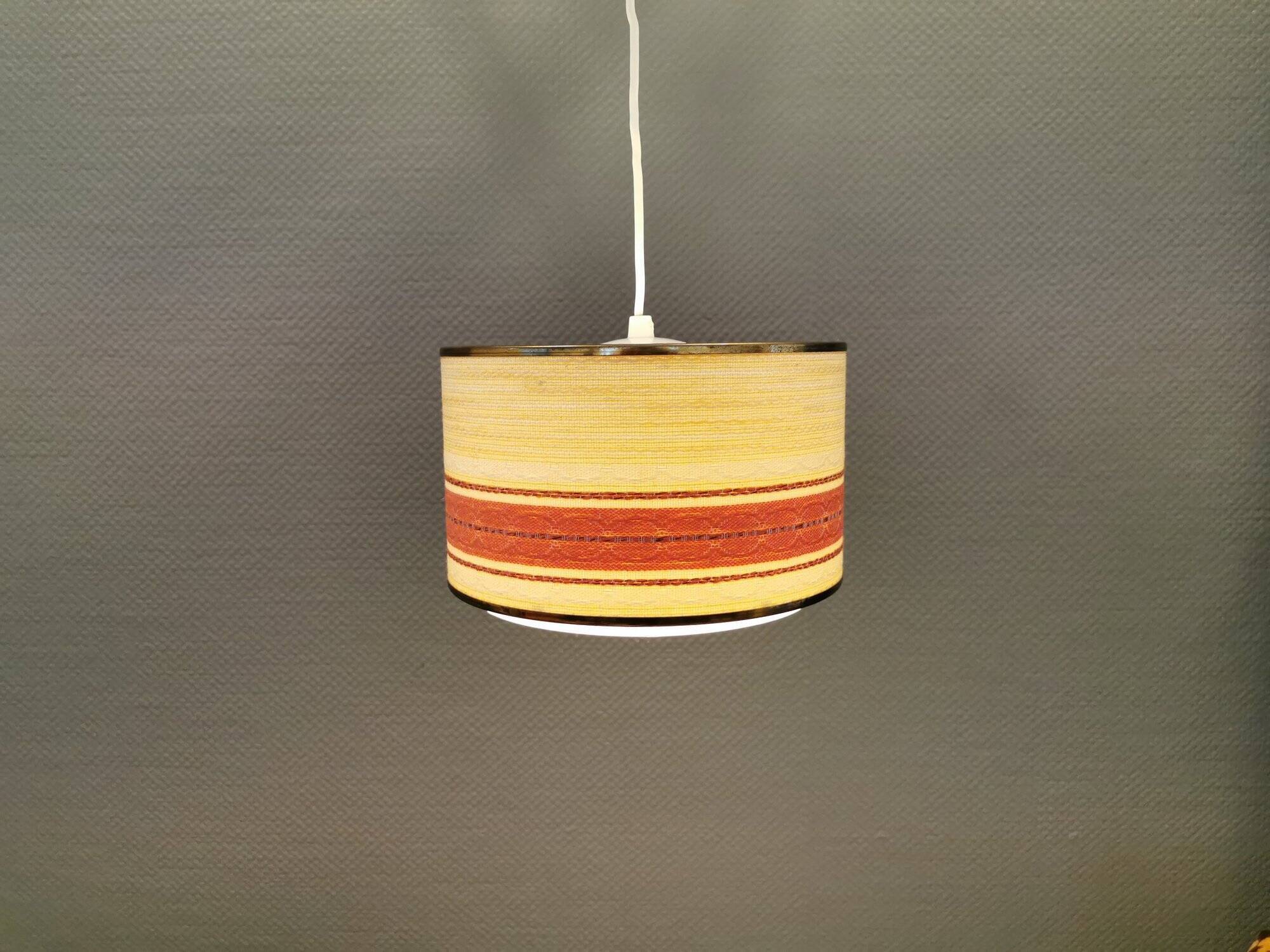Hanging lamp with brass-coloured details, made of fabric with intact plastic bottom grille.