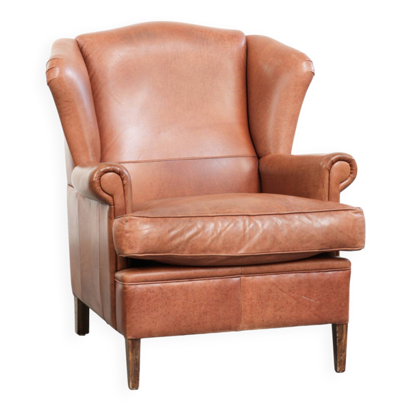 Fauteuil à oreilles en cuir de vache couleur cognac clair avec passepoil assorti.