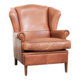 Fauteuil à oreilles en cuir de vache couleur cognac clair avec passepoil assorti.