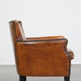 Cognac-colored sheepskin armchair with black piping and decorative nails