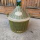 Large green glass lady-Jeanne in a khaki plastic basket, mid-century style.
