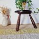 Small brutalist tripod stool made of turned wood.