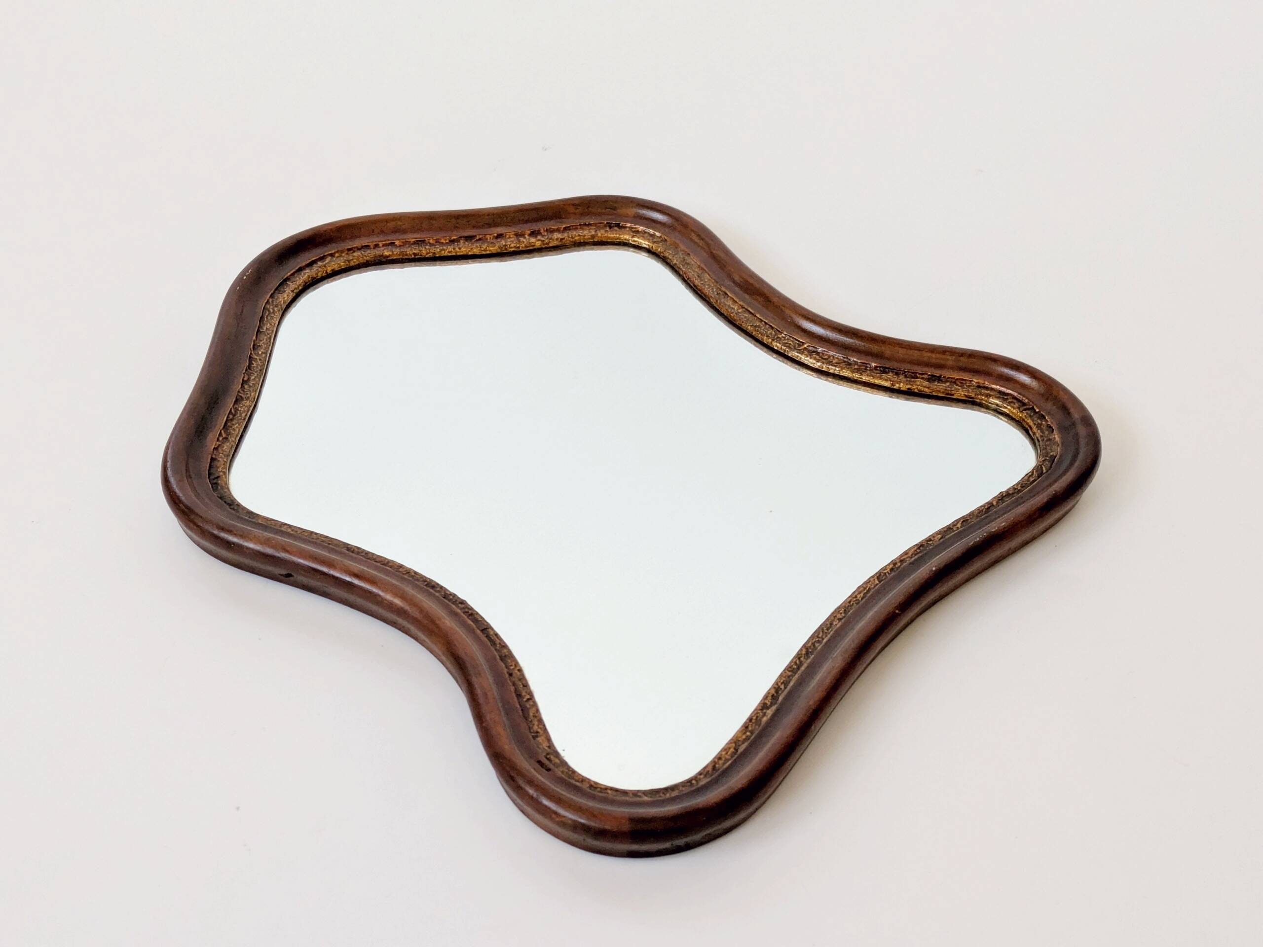 Antique wall mirror in carved wood with a wavy shape and a golden trim.