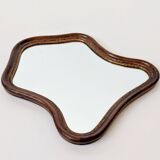 Antique wall mirror in carved wood with a wavy shape and a golden trim.
