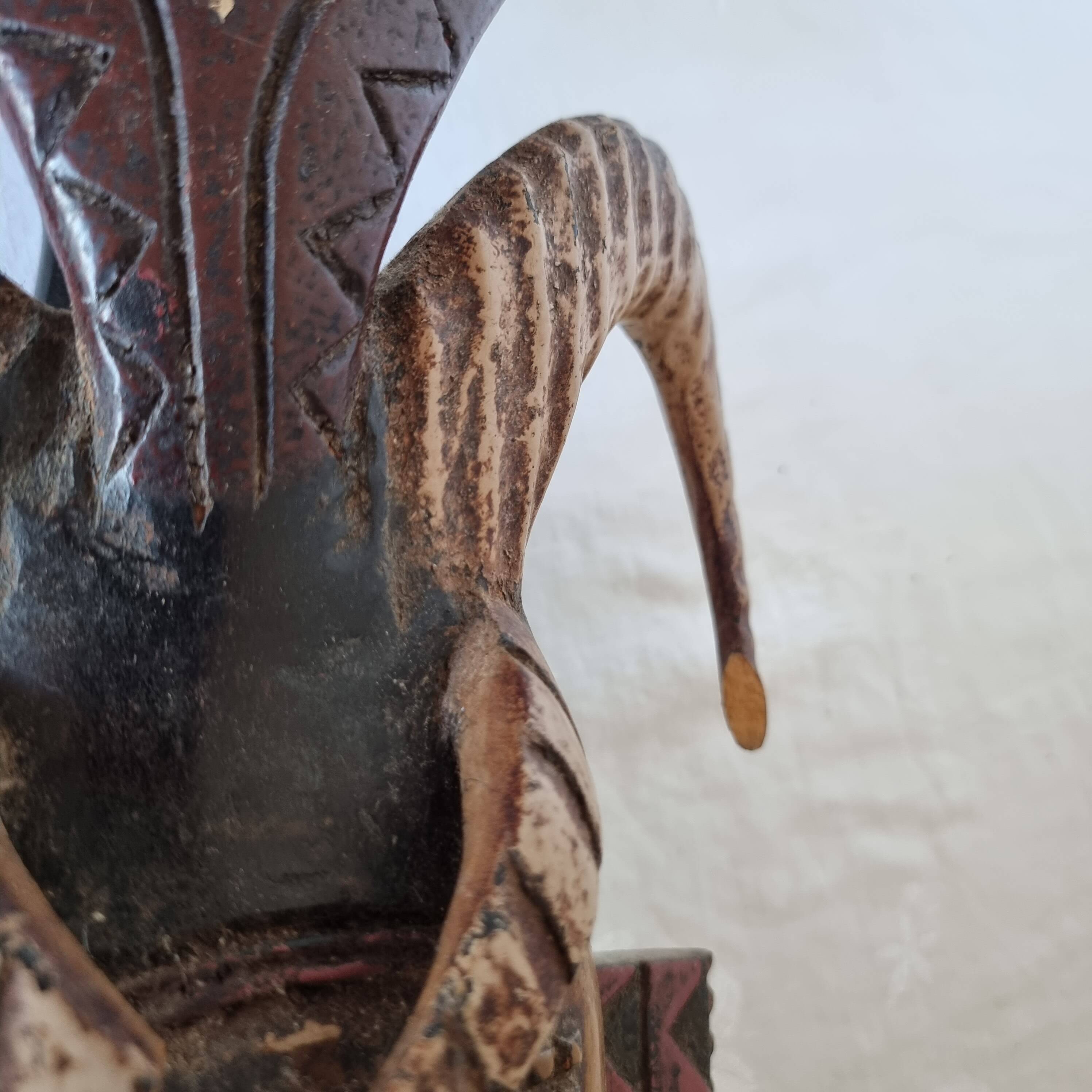 A large Senufo mask made of colored wood, decorated with an anthropomorphic figure