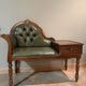 Antique carved wooden bench with green upholstered seat and backrest.