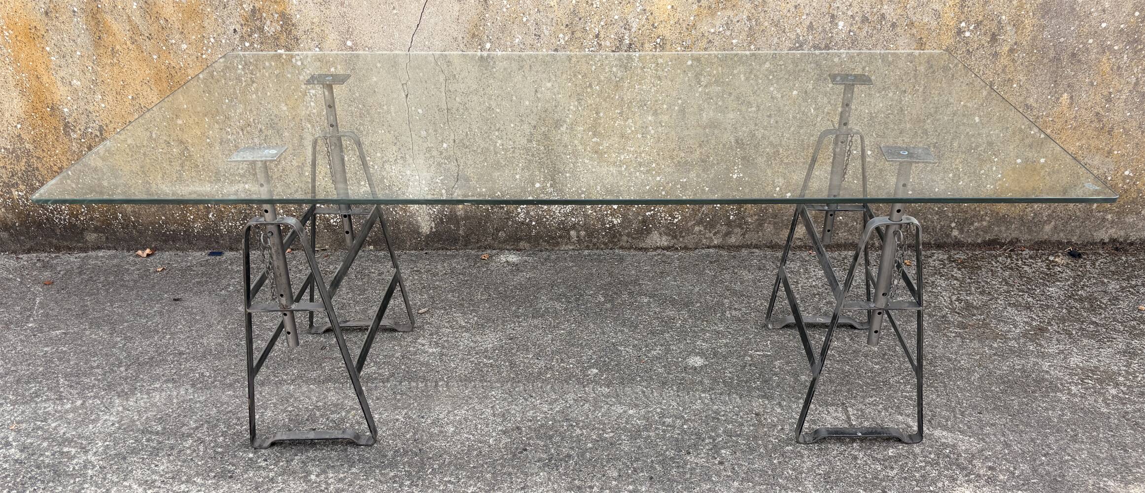 Large vintage industrial glass table with adjustable metal trestles.