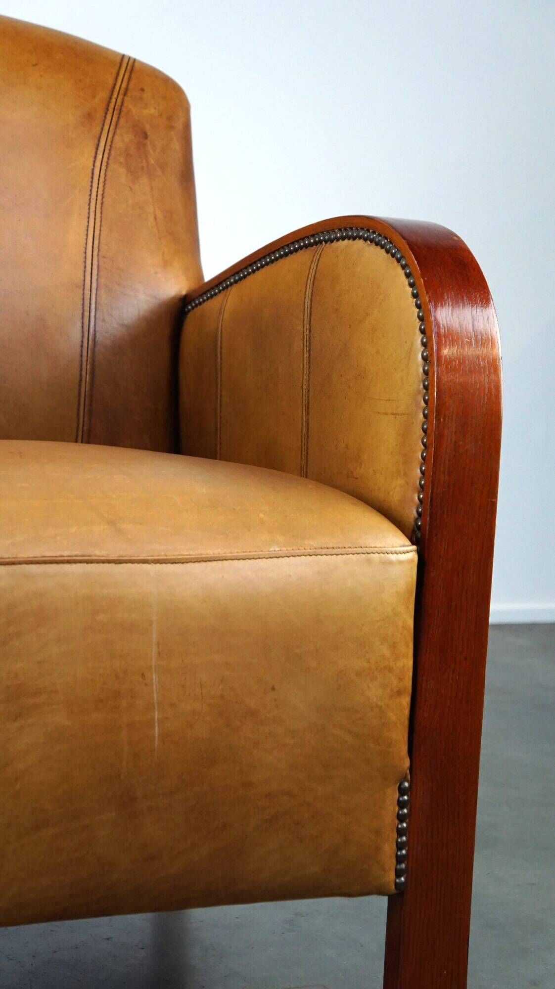 Luxurious cowhide Art Deco design armchair with wooden armrests and cognac-colored leather