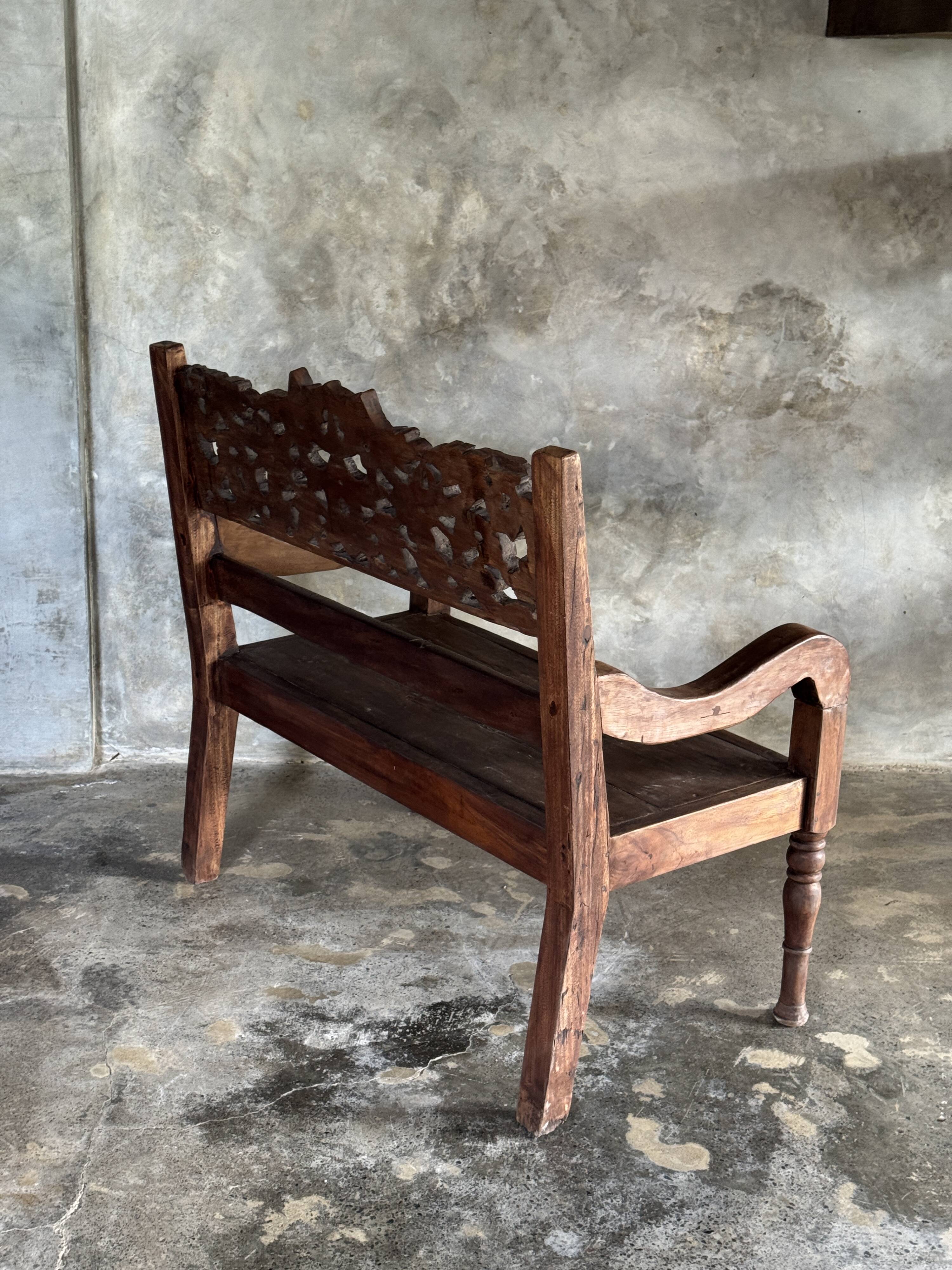 Small antique Indonesian bench in carved teak with plant and floral motifs.